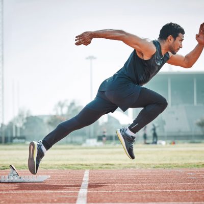 Stadium, man running and athlete on a runner and arena track for sprint race training. Fast, run and sports exercise of a male person in marathon for fitness and workout outdoor on a field for health.