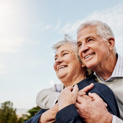 Sky, elderly couple and hug outdoors or happy in retirement or husband and wife in nature. Mature, man and woman smile in vacation or senior citizens care and embrace or date at the park for romance.